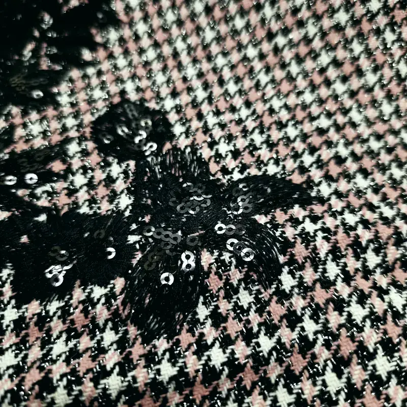 Κοντινό πλάνο του υφάσματος Tweed Πιε-ντε-Πουλ (Houndstooth) με μαύρο κέντημα λουλουδιών και πούλιες - Μοντέλο Chanel 54022, με εκλεπτυσμένο μοτίβο houndstooth σε μαύρο, λευκό και ροζ, διακοσμημένο με μαύρα πούλιες σε σχήμα λουλουδιών και περίτεχνο μαύρο κέντημα, που αποτυπώνει την ουσία των πολυτελών υφασμάτων. Υφάσματα Ιχτιάρογλου